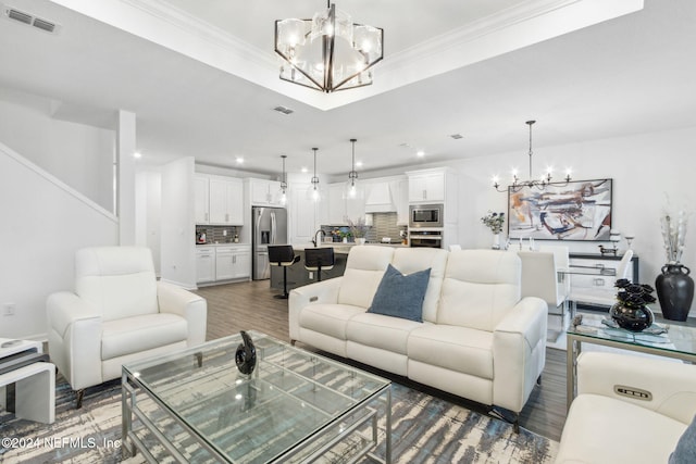 living room with dark wood-type flooring, ornamental molding, an inviting chandelier, and sink