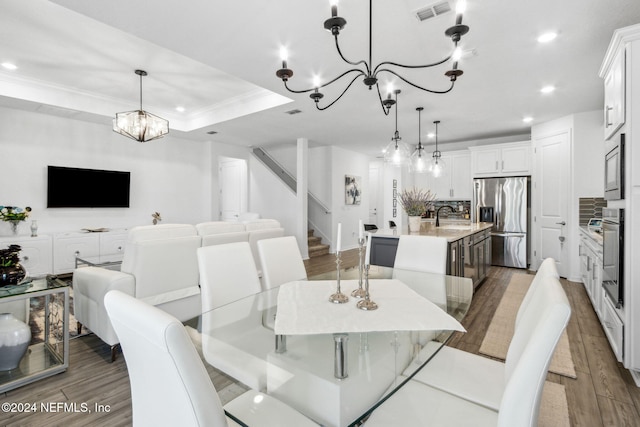 dining space with crown molding, an inviting chandelier, sink, a raised ceiling, and hardwood / wood-style flooring