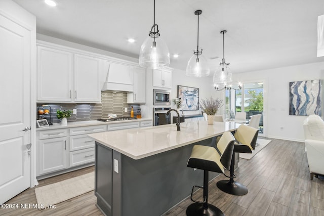 kitchen with decorative light fixtures, custom range hood, white cabinetry, and a kitchen island with sink