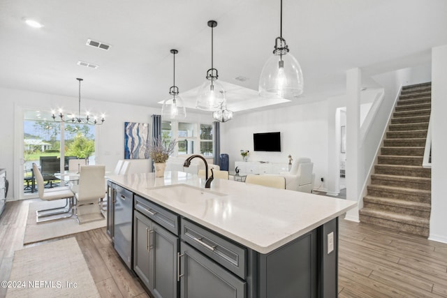 kitchen with pendant lighting, a notable chandelier, light hardwood / wood-style flooring, sink, and a center island with sink