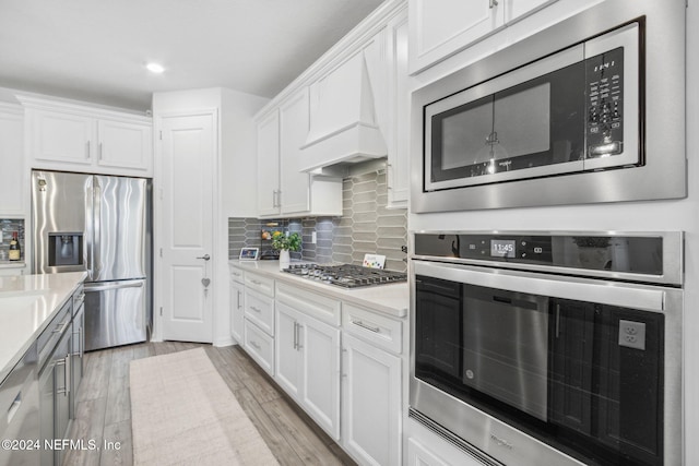 kitchen with appliances with stainless steel finishes, light hardwood / wood-style flooring, premium range hood, and white cabinets