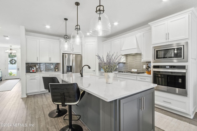 kitchen with stainless steel appliances, sink, premium range hood, pendant lighting, and a kitchen island with sink