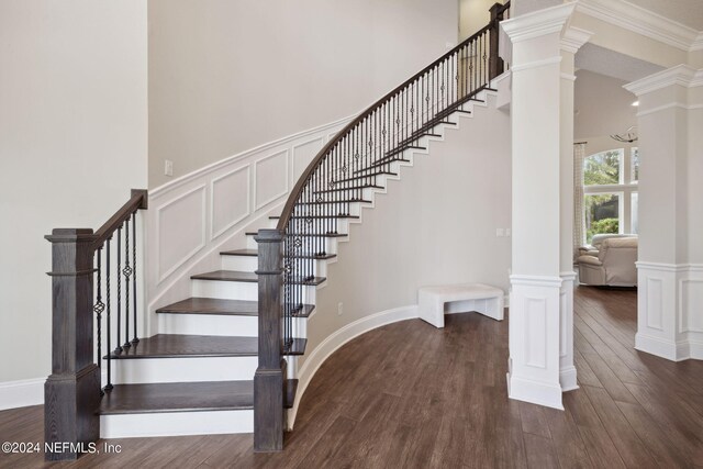 stairs featuring wood-type flooring, crown molding, and ornate columns