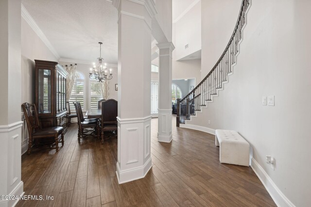 interior space with dark wood-type flooring, decorative columns, a chandelier, and ornamental molding