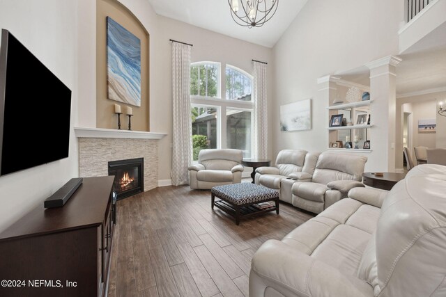 living room with an inviting chandelier, a stone fireplace, wood-type flooring, decorative columns, and high vaulted ceiling