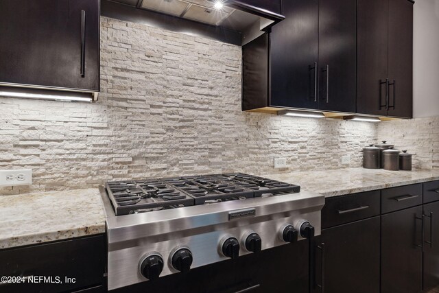 kitchen with backsplash, stainless steel cooktop, light stone counters, premium range hood, and dark brown cabinets