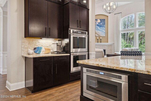 kitchen with appliances with stainless steel finishes, light hardwood / wood-style floors, a notable chandelier, and a stone fireplace