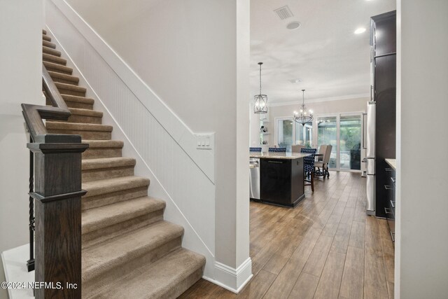 stairway featuring ornamental molding, an inviting chandelier, and wood-type flooring