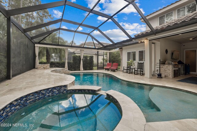 view of swimming pool with a patio area, an in ground hot tub, exterior kitchen, area for grilling, and glass enclosure