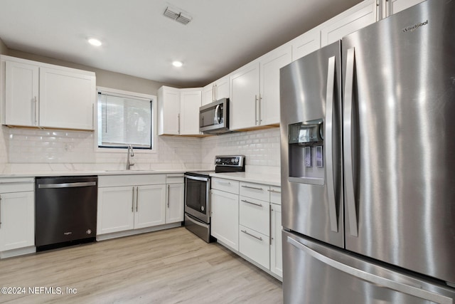 kitchen with sink, backsplash, white cabinetry, stainless steel appliances, and light hardwood / wood-style floors