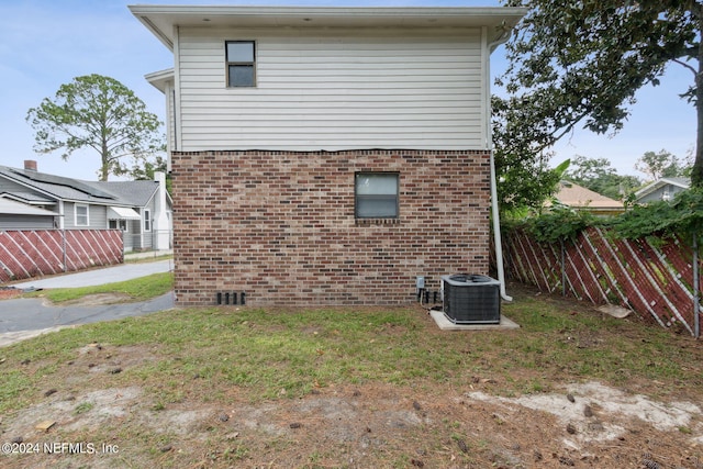 view of side of property featuring fence, a yard, central AC unit, and brick siding