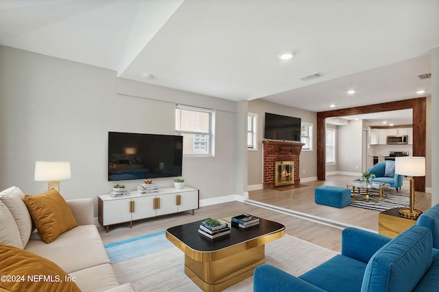 living area with a wealth of natural light, a brick fireplace, baseboards, and wood finished floors