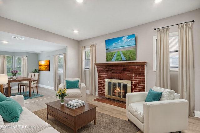 living area with light wood finished floors, visible vents, a brick fireplace, and plenty of natural light