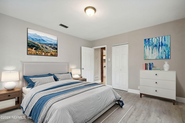 bedroom with light wood-type flooring, visible vents, a closet, and baseboards