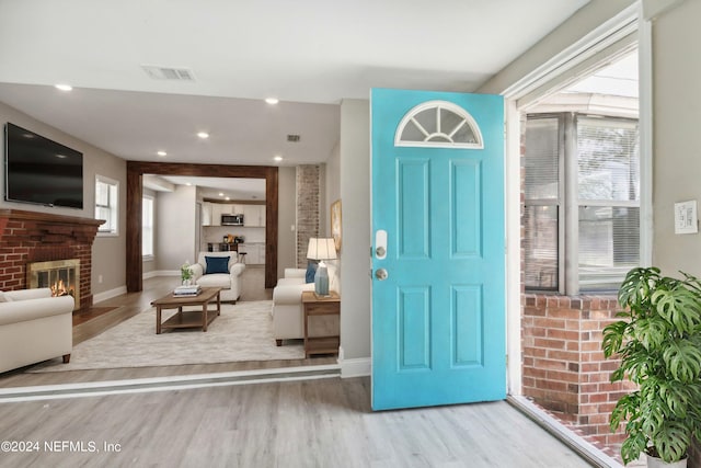 entrance foyer with light wood-style flooring, baseboards, a brick fireplace, and visible vents