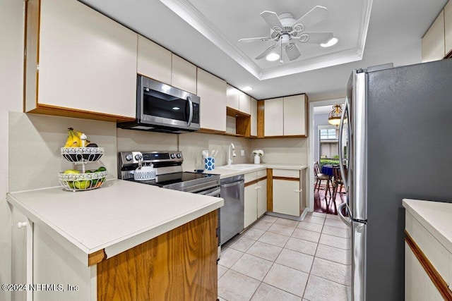 kitchen with appliances with stainless steel finishes, ornamental molding, a tray ceiling, ceiling fan, and white cabinetry