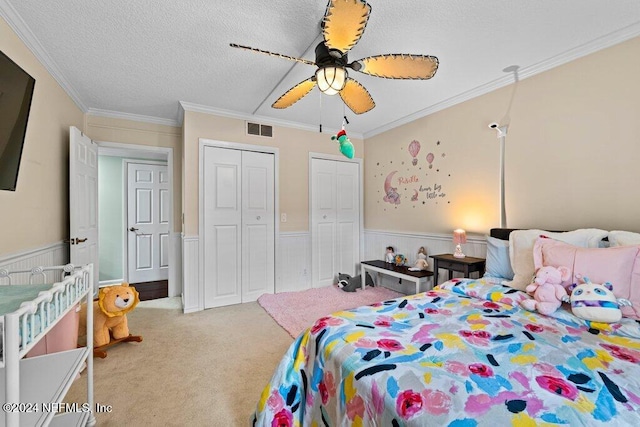 bedroom featuring carpet, two closets, crown molding, ceiling fan, and a textured ceiling