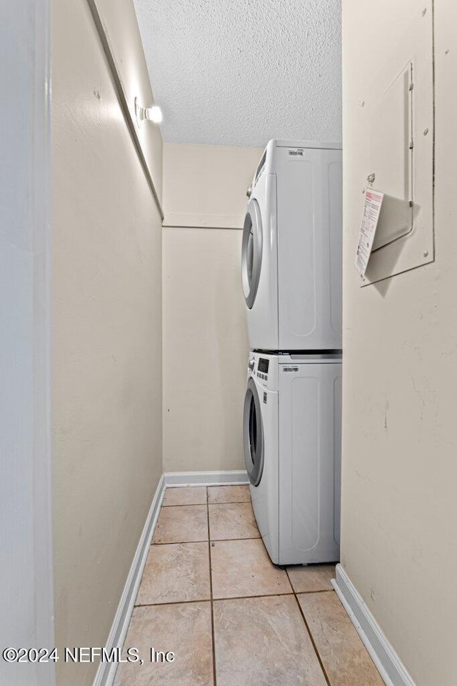 clothes washing area with electric panel, light tile patterned flooring, stacked washing maching and dryer, and a textured ceiling