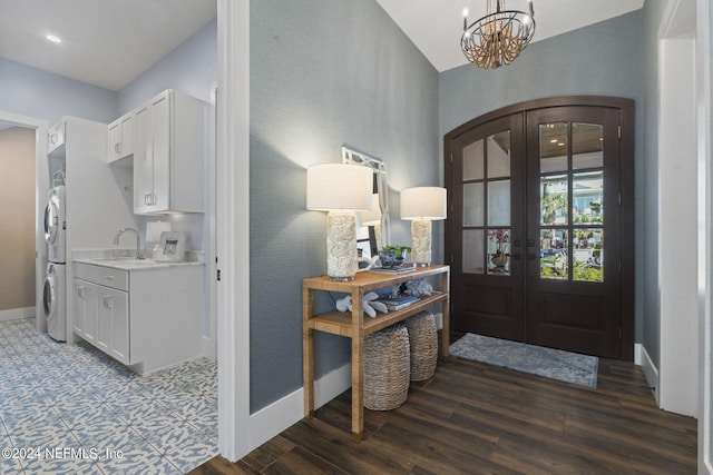 foyer entrance with an inviting chandelier, wood-type flooring, french doors, stacked washer and dryer, and sink