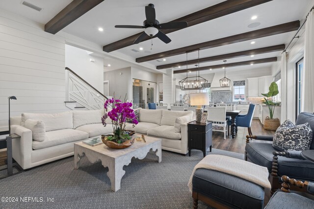 living room featuring ceiling fan with notable chandelier, beamed ceiling, wooden walls, and dark hardwood / wood-style flooring