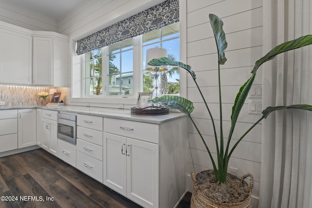 kitchen with dark wood-type flooring, stainless steel microwave, backsplash, and white cabinets