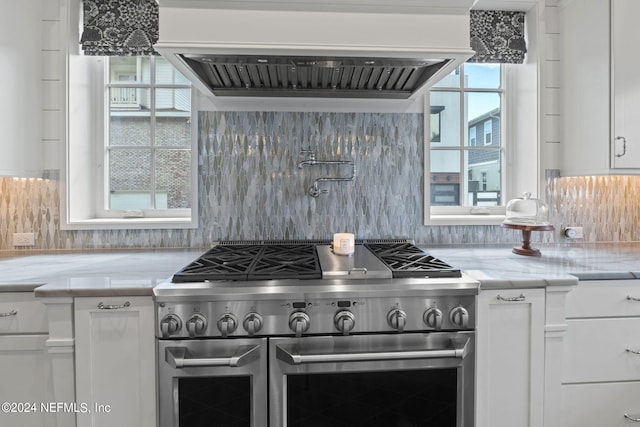 kitchen with white cabinetry, custom range hood, range with two ovens, and tasteful backsplash