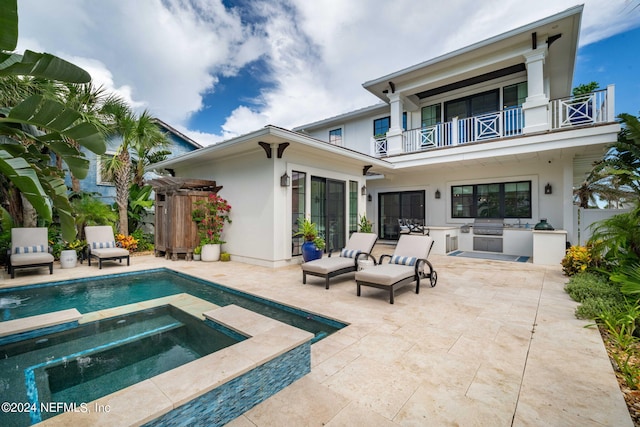 back of property featuring a balcony, an in ground hot tub, an outdoor kitchen, and a patio