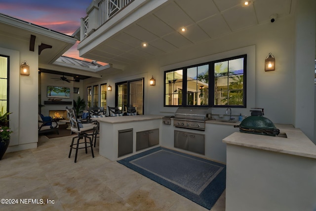 patio terrace at dusk with ceiling fan, an outdoor wet bar, an outdoor kitchen, and area for grilling