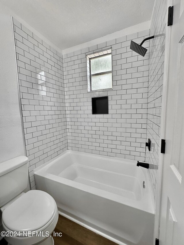 bathroom with a textured ceiling, tiled shower / bath combo, and toilet