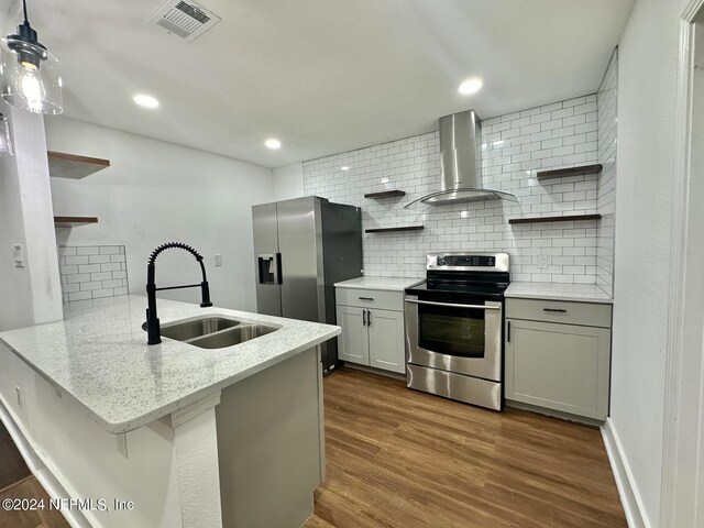 kitchen featuring kitchen peninsula, stainless steel appliances, sink, wall chimney range hood, and dark hardwood / wood-style floors