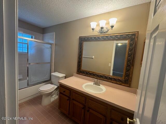 full bathroom featuring tile patterned flooring, a textured ceiling, toilet, shower / bath combination with glass door, and vanity