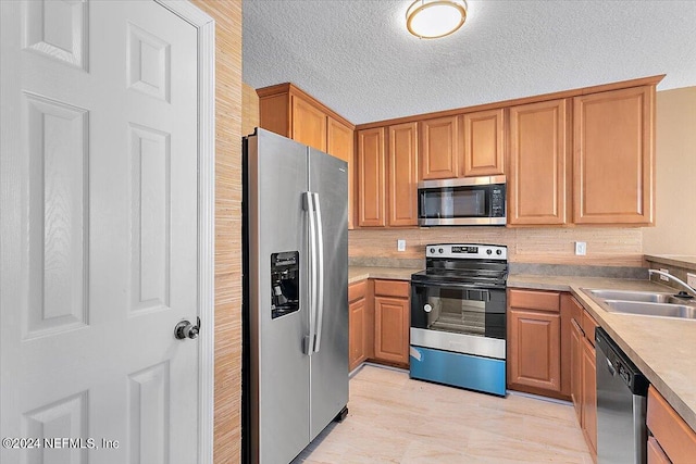 kitchen with brown cabinetry, stainless steel appliances, a sink, and light countertops