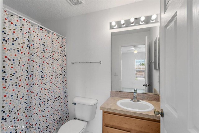 bathroom featuring a textured ceiling, vanity, curtained shower, ceiling fan, and toilet