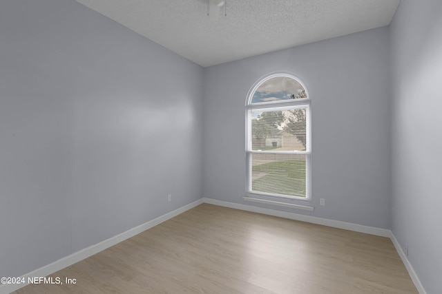 unfurnished room featuring light wood-style floors, baseboards, and a textured ceiling