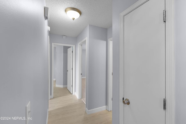 corridor featuring light wood-type flooring, baseboards, and a textured ceiling