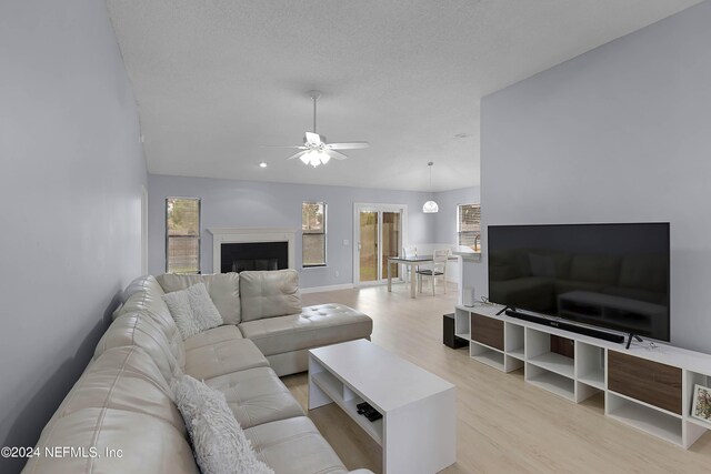 living room with ceiling fan, light wood-type flooring, a textured ceiling, and lofted ceiling