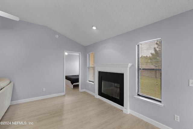 unfurnished living room with light hardwood / wood-style floors, a textured ceiling, and vaulted ceiling