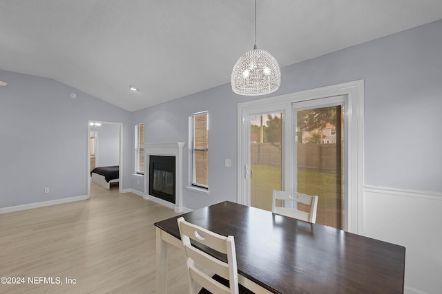 dining area featuring baseboards, a glass covered fireplace, lofted ceiling, an inviting chandelier, and light wood-type flooring