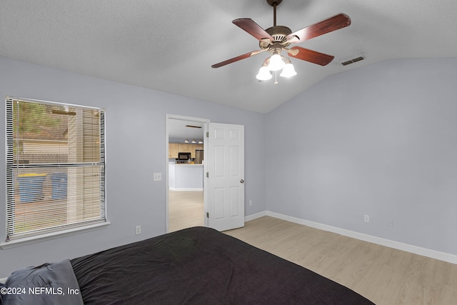 unfurnished bedroom featuring a textured ceiling, light wood-type flooring, vaulted ceiling, and ceiling fan