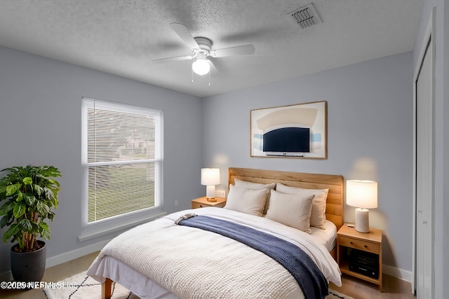 bedroom with a textured ceiling, light wood-style flooring, visible vents, and baseboards