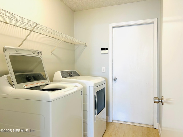 clothes washing area featuring laundry area, a textured ceiling, washer and clothes dryer, and light wood-style floors