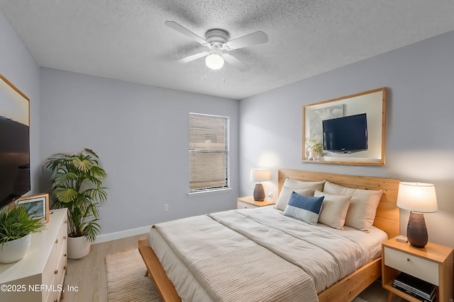 bedroom with a ceiling fan, a textured ceiling, baseboards, and wood finished floors