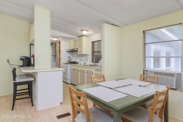 kitchen featuring cream cabinetry, kitchen peninsula, vaulted ceiling, white gas range, and light hardwood / wood-style floors