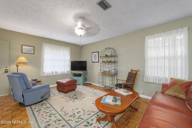 living room with parquet floors, ceiling fan, and a textured ceiling