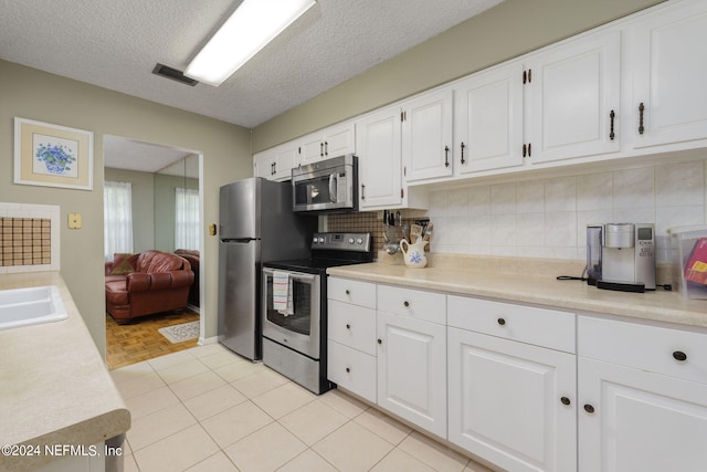 kitchen featuring appliances with stainless steel finishes, a textured ceiling, white cabinets, and tasteful backsplash