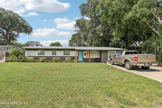 ranch-style home featuring a front lawn, fence, concrete driveway, metal roof, and brick siding