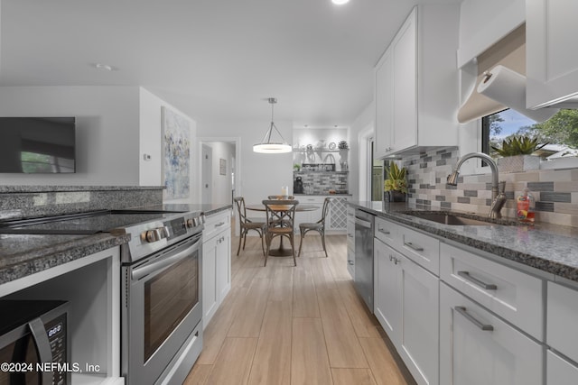 kitchen with a sink, dark stone countertops, white cabinetry, stainless steel appliances, and decorative backsplash