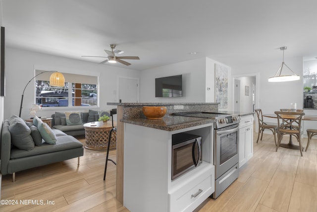 kitchen featuring open floor plan, white cabinetry, stainless steel appliances, dark stone counters, and light wood-style floors