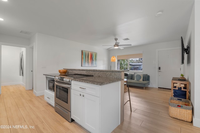 kitchen with a breakfast bar, light hardwood / wood-style flooring, electric stove, ceiling fan, and white cabinets