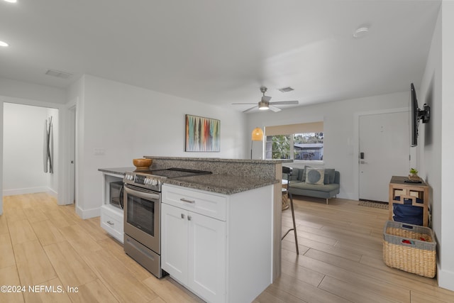 kitchen featuring dark stone countertops, a breakfast bar area, wood finish floors, electric range, and white cabinets